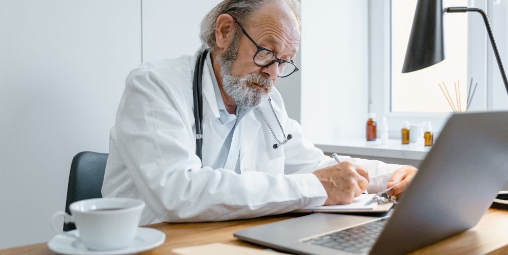 doctor making notes and looking at laptop