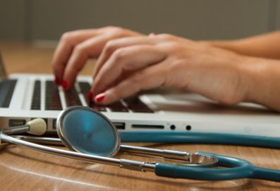 person typing on laptop next to stethoscope
