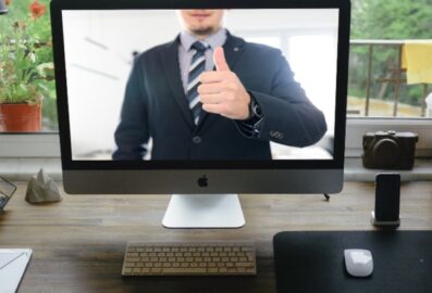 person wearing a suit holding thumbs up on video call