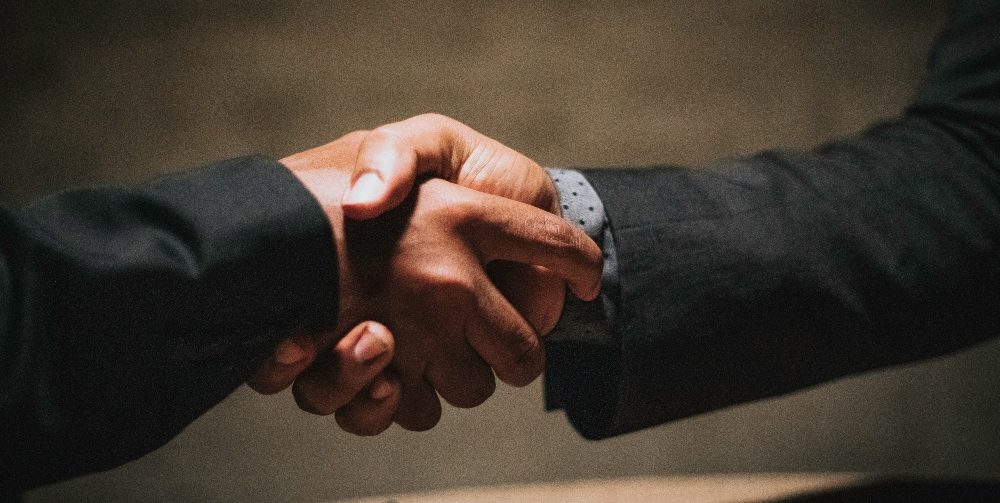 two people wearing black suits shaking hands