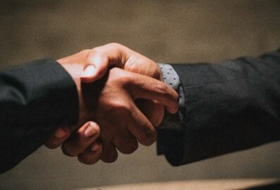 two people wearing black suits shaking hands